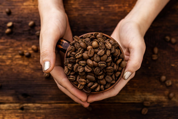 咖啡豆在一个杯子在一个棕色的背景女性手中。图片下载