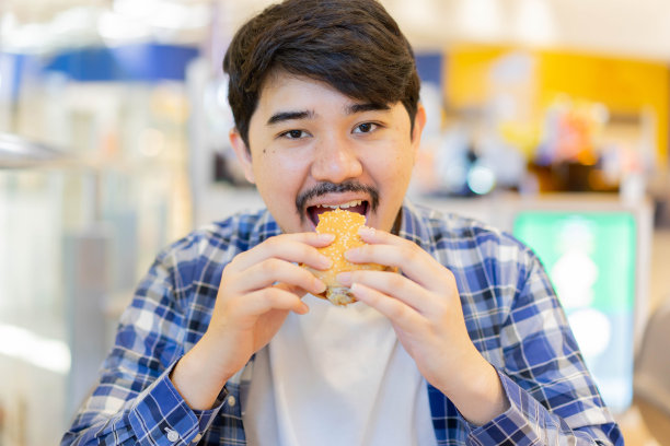 年轻中东男人在餐厅享用早午餐，快乐地咬汉堡，休闲度周末，快餐和人们的生活方式概念图片下载