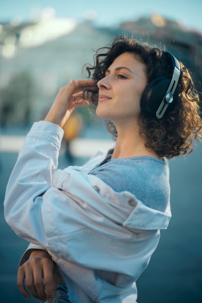 一位留着卷发的年轻女子站在街上听音乐。图片下载
