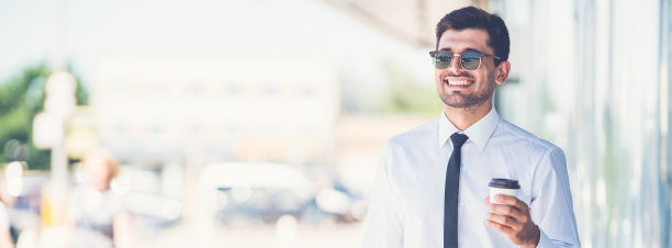 戴墨镜的商人端着咖啡，提着行李箱走着图片下载