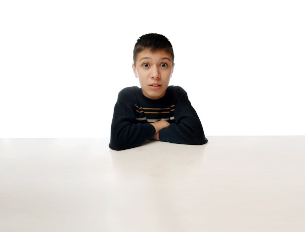 一个惊讶的小男孩坐在一张白色背景的大桌子旁图片下载
