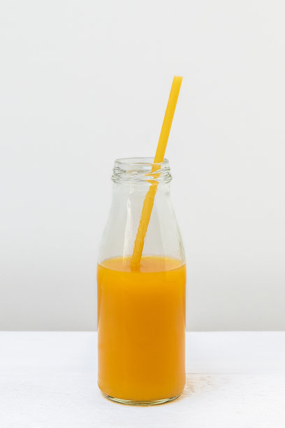 玻璃瓶与果汁和意大利面吸管在光背景，垂直图像图片下载