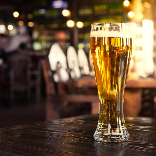 在酒吧或酒吧的桌子上放一杯冰镇啤酒。模糊的酒吧灯光背景。图片下载