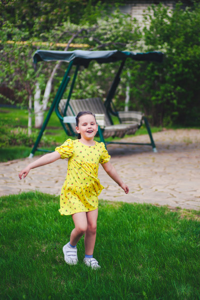 一个笑着的女孩在夏天的后院跳舞，背景是花园秋千，享受着温暖的一天图片下载