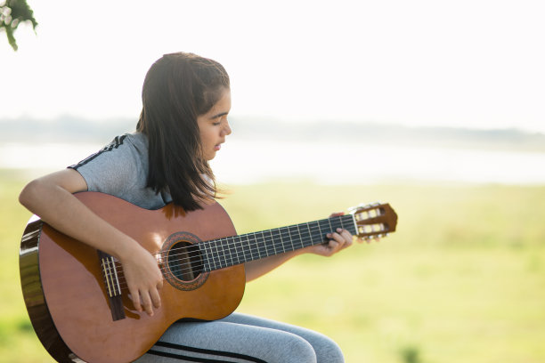 可爱的女孩，弹吉他，唱歌，音乐或幸福概念，日落温暖的光色调效果。图片下载