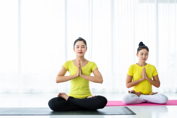 两个年轻的亚洲女性锻炼练习瑜伽在黄色的裙子或姿势与教练和练习冥想健康的生活方式和健康健身的概念在一个健身房。图片下载