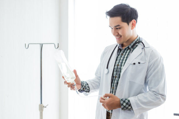 亚洲青年医生的肖像治疗建议微笑的脸与听诊器与生理盐水瓶在医院的背景。图片下载