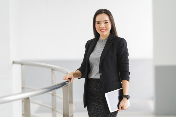 这是一幅乐观自信的亚洲女商人的肖像，她穿着商务套装，站在办公大楼里使用数码平板电脑。商业库存图片图片下载