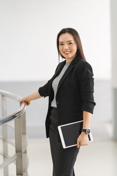 这是一幅乐观自信的亚洲女商人的肖像，她穿着商务套装，站在办公大楼里使用数码平板电脑。商业库存图片图片下载