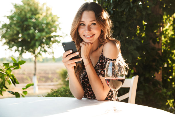 女士坐在公园外的咖啡馆里喝着酒，用手机聊天。图片下载