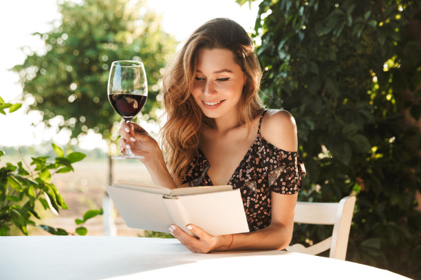 美丽的年轻女子拿着酒杯喝葡萄酒。图片下载