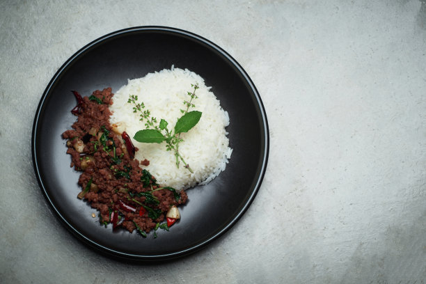 自制泰式辣炒罗勒牛肉末配泰国茉莉花饭黑色碟上放着赤裸裸的灰色混凝土纹理
餐桌的一边有小的免费复制空间图片下载