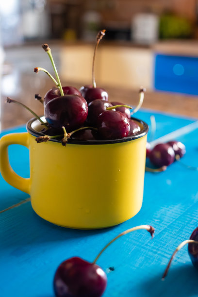 蓝色桌子上，黄色咖啡杯里的樱桃，简约主义的照片图片下载