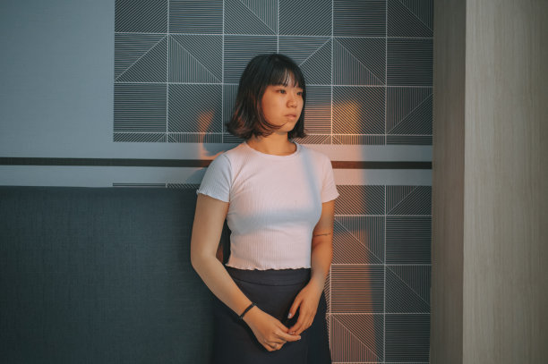 肖像悲伤的亚洲华人少女站在卧室墙前，夕阳的光从窗户照在脸上图片下载