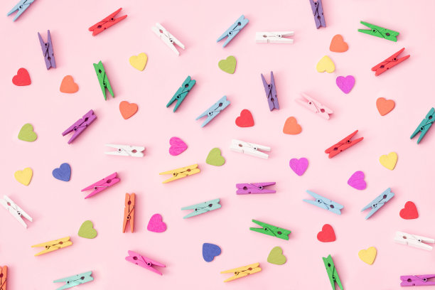 小的彩色木制洗衣钳与彩色的木心安排在粉红色的背景。图片下载