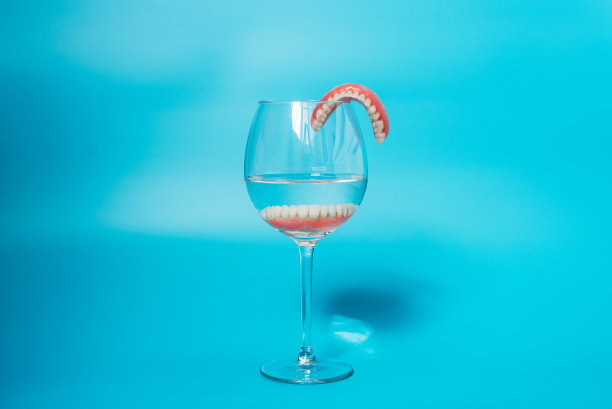 假牙齿保健。下颌的可活动的塑料假牙。一组假牙放在一个蓝色背景的水里。两个丙烯酸假牙。假牙或假牙，特写。本空间图片下载