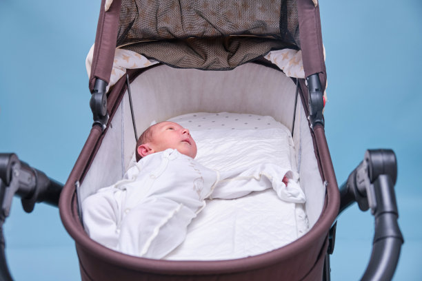 蓝色背景下婴儿车里的小男孩。一个穿着白色衣服只用尿布的孩子躺在婴儿车里，摄影棚拍摄图片下载