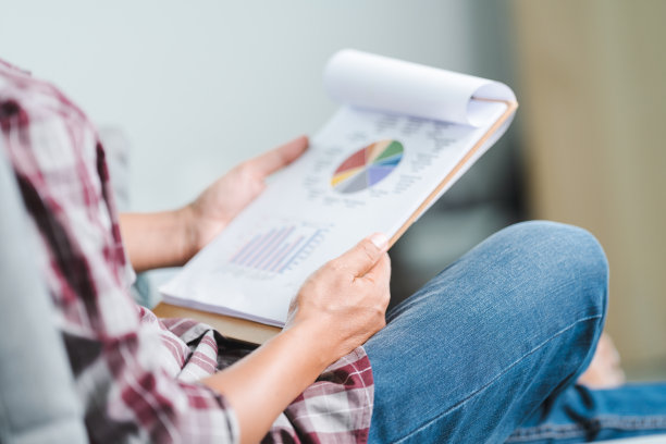 近距离拍摄的一个商人穿着休闲看商业报告的文件和智能手机，而坐在沙发上放松的姿势在家庭办公室。商业库存图片图片下载