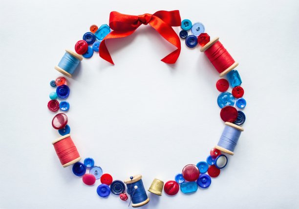 花环是由红色和蓝色的纽扣和线和别针和一个明亮的缎带蝴蝶结在顶部。在白色背景和复制空间。工艺、缝纫和刺绣的概念图片下载