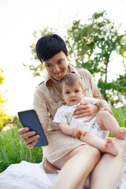 一名年轻女子带着小儿子坐在绿色草坪上自拍图片下载