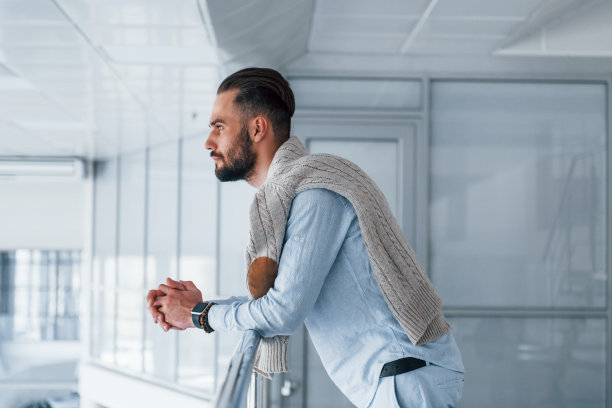 靠在银色的栏杆上。年轻英俊的男人白天在办公室里穿着正式的衣服图片下载