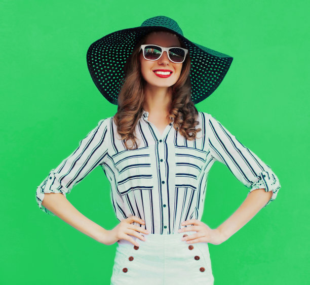 美丽的年轻女子的肖像戴着黑色圆形的夏季帽子，白色条纹衬衫在绿色的背景图片下载