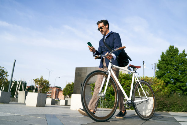 成年男性上班的时候，一只手拿着自行车，另一只手看手机。环保交通工具的概念图片下载