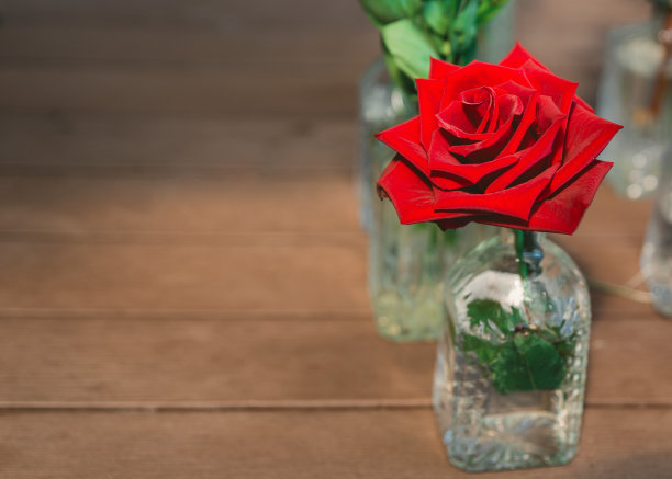 猩红色的玫瑰花蕾在装饰瓶上的木制背景。漂亮的玫瑰在花瓶和复制空间。浪漫的碎花背景。图片下载