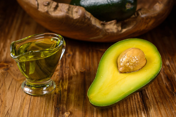 一半牛油果和牛油果油装在一个玻璃碗里放在破旧的桌子上。健康饮食、饮食保养、身体保养和护发理念。图片下载