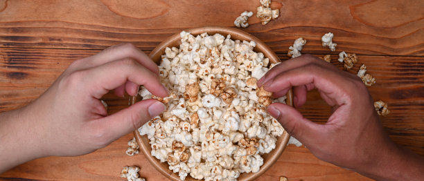 两个男人从木桌上的桶里拿爆米花。图片下载