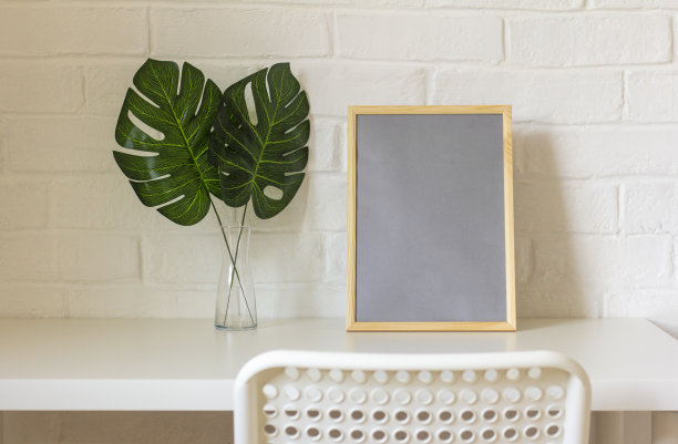 一个家工作场所。桌子上有一个空的相框或照片，还有插在花瓶里的怪物树叶。北欧风格。图片下载