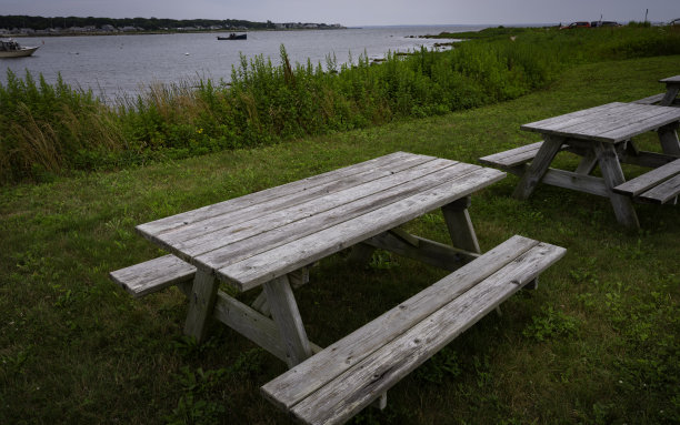 风化的木制公园桌子与沙滩草坪上的座位。复古风格的自然海景背景图像与空间的文字或设计。图片下载