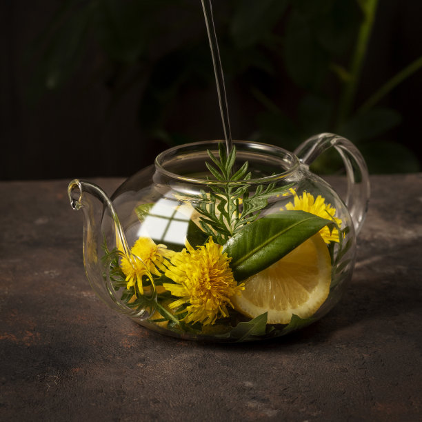 茶在玻璃茶壶与香草，鲜花和柠檬片在黑暗的背景图片下载