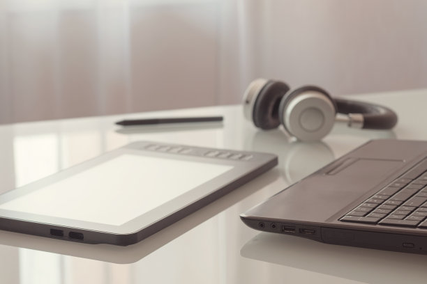 玻璃桌上放着一台图形平板电脑、笔记本电脑和耳机。图片下载