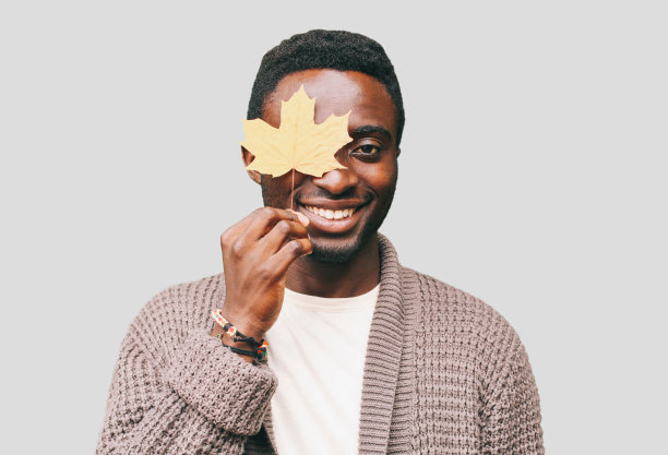 一个快乐微笑的非洲人的肖像与秋天的黄色枫叶在灰色的背景图片下载