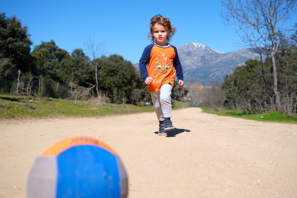 一个男孩在泥土路上追着一个球跑图片下载
