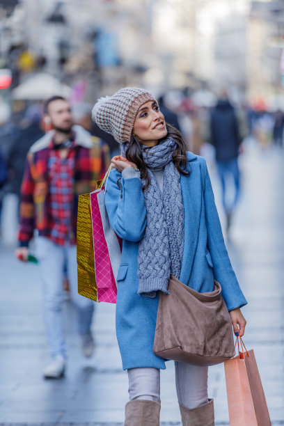 一个快乐的女人的肖像谁走在购物袋通过城市的街道。图片下载