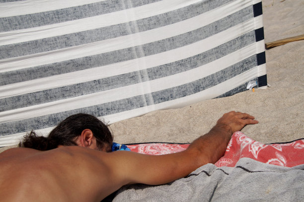 日光浴，在海滩上放松。在海滩上晒太阳的男性。人们在海边享受炎热的夏天。图片下载