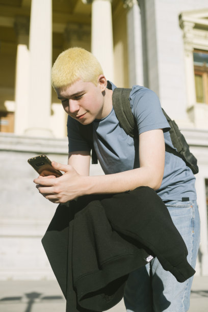 背包里穿着运动衫的少年靠在滑板上用手机打字图片下载