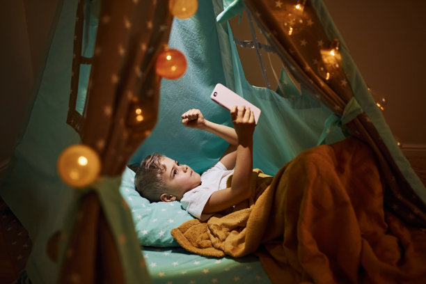使用手机。傍晚时分，穿着便服的小男孩躺在帐篷里图片下载