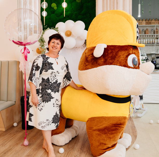 一位老妇人站在一个儿童节日的成长娃娃旁边。图片下载