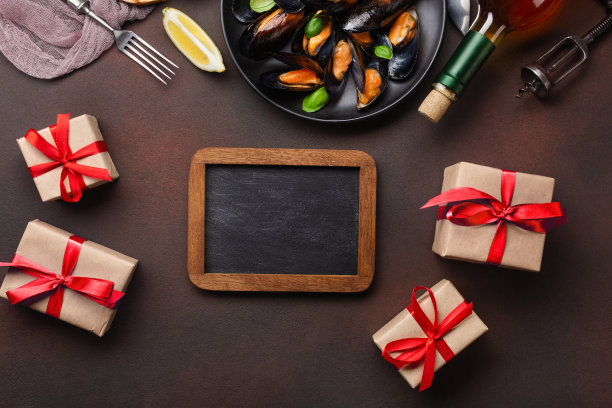 海鲜贻贝和罗勒叶在一个黑色盘子，叉子，刀，粉笔板和礼品盒在毛巾和生锈的背景图片下载