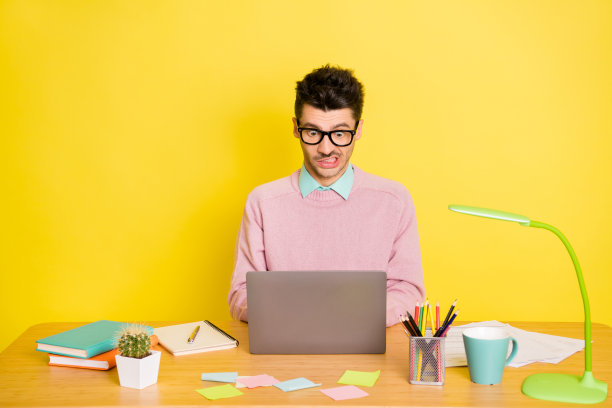 照片的年轻不高兴沮丧的男人在眼镜工作打字在桌子上的笔记本电脑孤立在黄色的背景图片下载