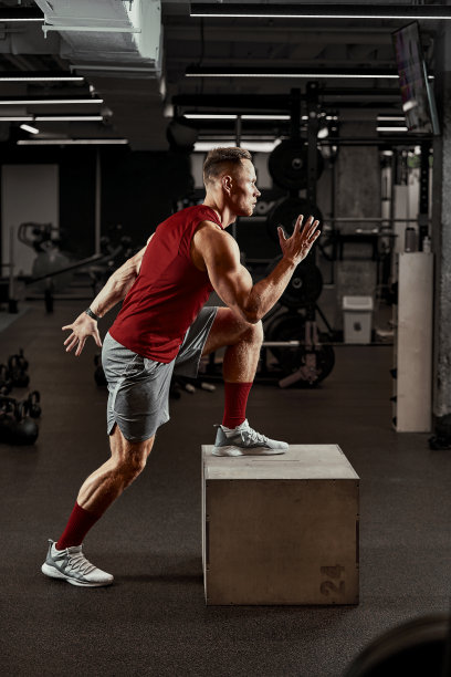 性感的肌肉男使用平台为他的腿在一个黑暗的彩色背景的健身房图片下载