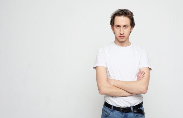 年轻英俊的男子穿着白色t恤交叉双手，看着相机在灰色的背景图片下载