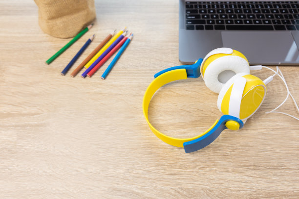 用电脑笔记本电脑的拷贝空间、耳机和彩色铅笔放在木桌上的俯视图拍摄，展示了学生孩子可以通过互联网技术在家学习的在线教育理念。图片下载
