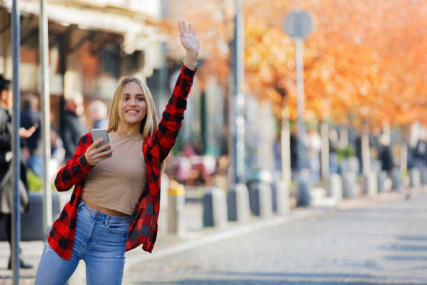 一位年轻女子站在街上挥动手臂想要搭出租车。图片下载