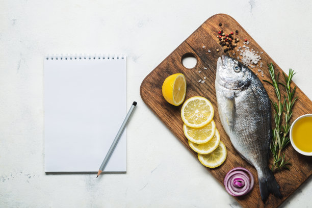 新鲜生的剑鱼放在一个带有香料的质朴的木制砧板上，还有一个食谱或菜单的笔记本。图片下载