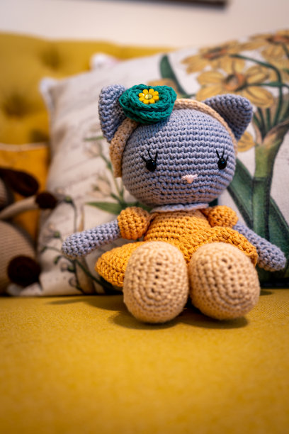 Amigurumi毛绒玩具坐在黄色的沙发上，背景是其他手工玩具。图片下载