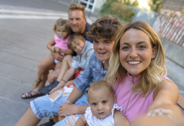 年轻人坐在户外的长椅上享受家庭时光。妈妈和爸爸肖像假日与孩子参观城市中心。快乐的假期自拍。快乐与生活理念图片下载